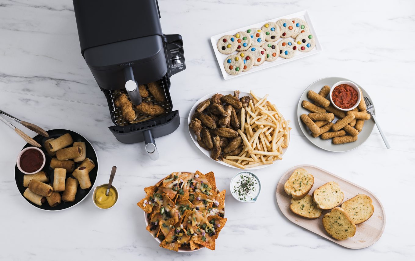 Ninja DoubleStack XL SL401 two-basket air fryer with both stacked drawers open beside plates of party food