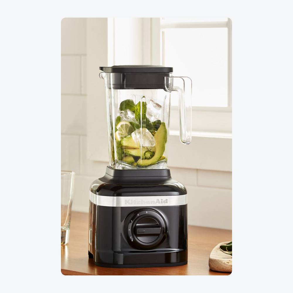 KitchenAid K150 blender in black with avocado, greens, and ice in its 48-ounce jar on a kitchen counter