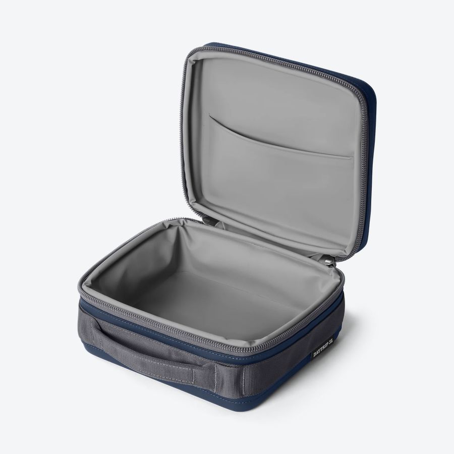 YETI Daytrip 3L Lunch Box in Navy, open three-quarter studio view showing the gray liner and internal PackAttic pocket, DAYTRIP 3L label visible